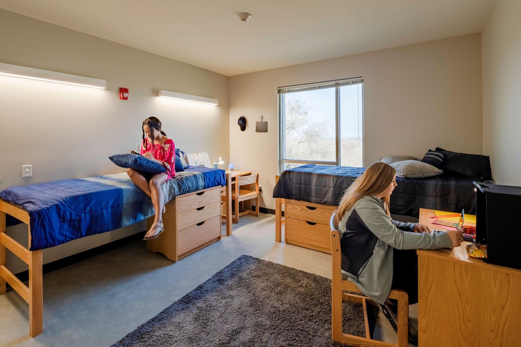 Inside of dorm room with two students studying. Viewing window, two beds, two desks